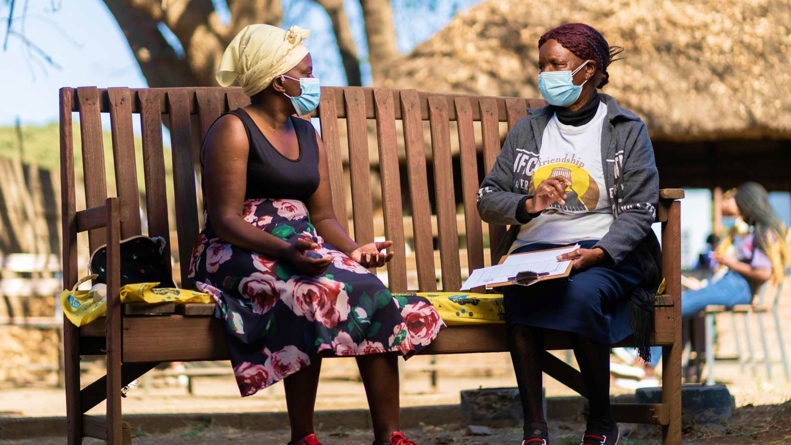 Two women sitting on a bench wearing face masks.