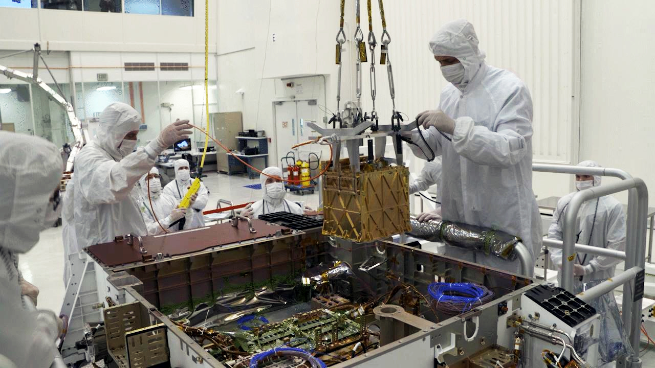 NASA engineers lowering a golden box into the Perseverance rover