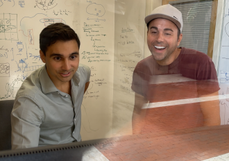 Two men smiling in front of a whiteboard.