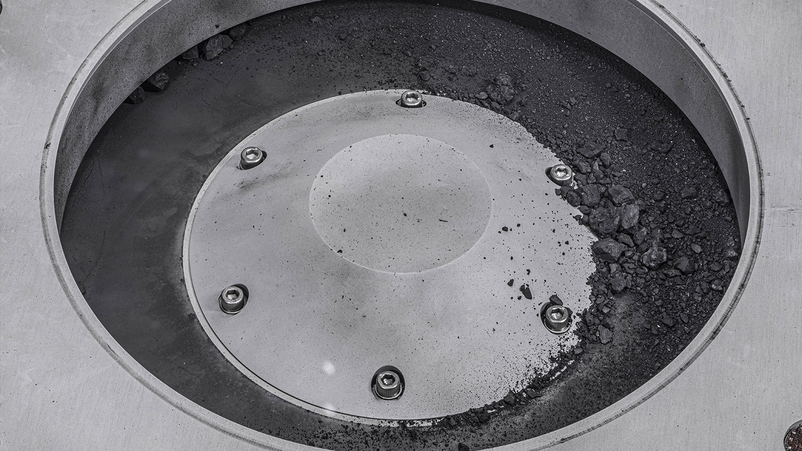 A close up of a metal container with bits of the Bennu asteroid sample on it