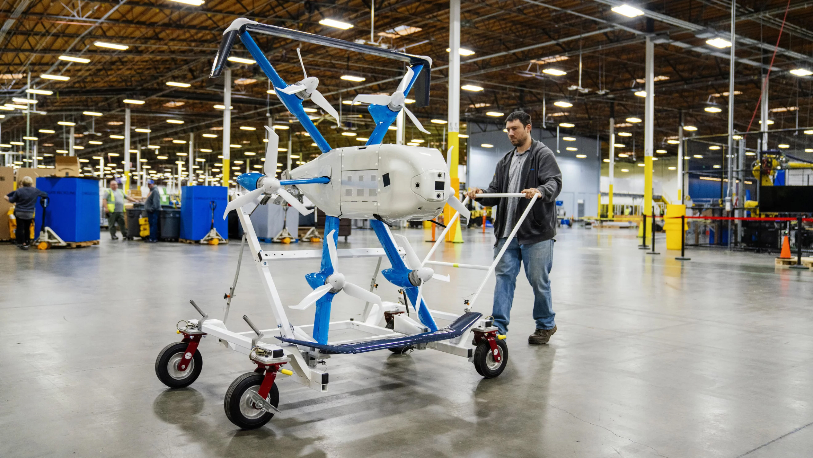 An Amazon worker with one of the new Prime Air drones on a cart in a warehouse