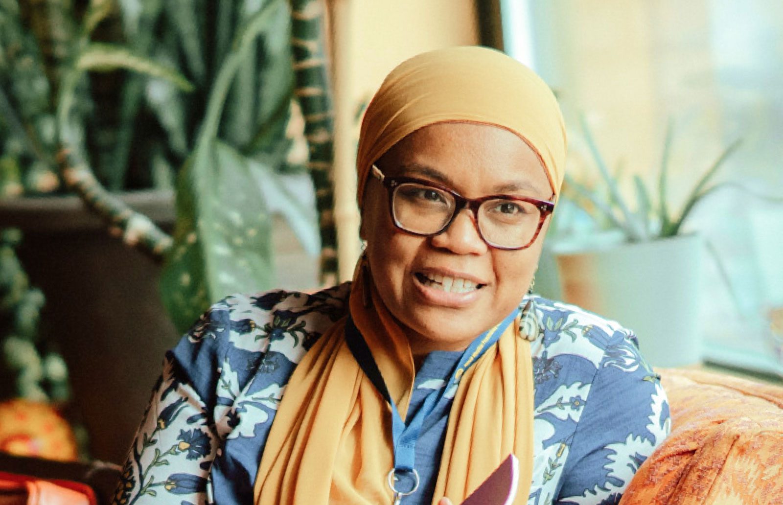 A woman wearing a hijab sitting on an orange couch.