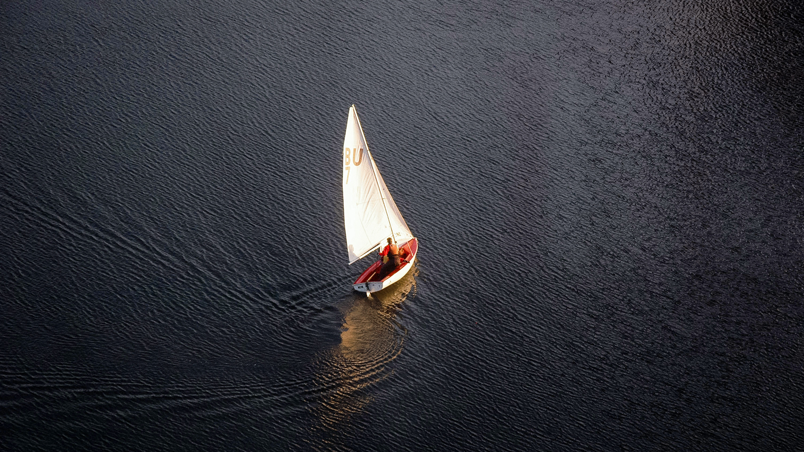 An aerial view of a sailboat peacefully sailing on a body of water, providing solitude and tranquility for individuals seeking mental health.