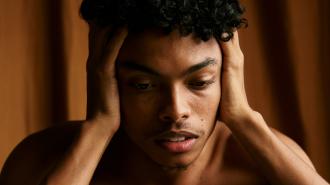 A young black man with anxiety, holding his head in distress.