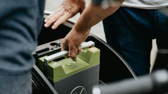 A person is putting a battery into the back of a bike.