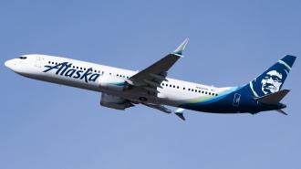 An alaska airlines boeing 737 ascending against a clear blue sky.