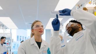 Two scientists in lab coats and safety goggles examining a medical device