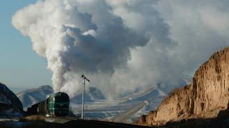 A fusion energy locomotive emits a large plume of smoke as it travels through a rugged, mountainous landscape.