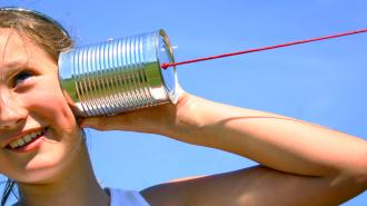 A person holds a tin can with a red string connected to it up to their ear.