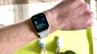 A person’s wrist wearing a smartwatch displaying a high-intensity interval training workout screen. Among smart health devices, this one stands out with its clarity and ease of use. Green exercise mat and white sneakers are visible in the background.