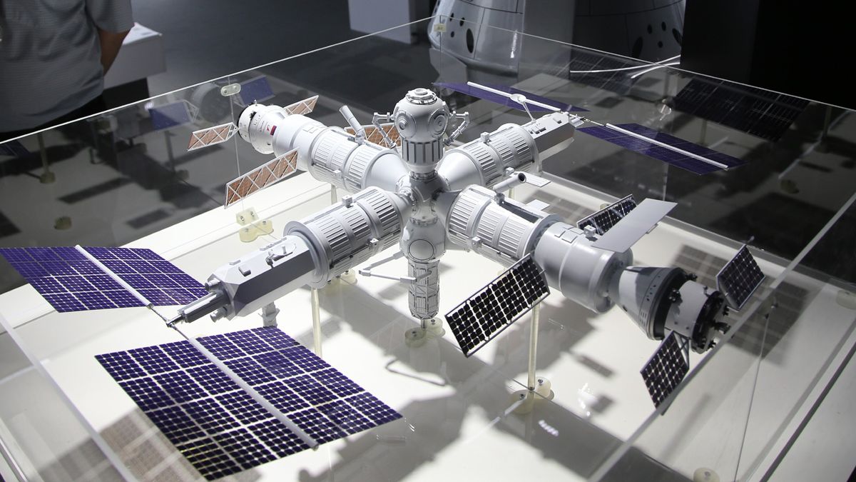 A model of a space station with multiple modules and solar panels on display in a brightly lit room.