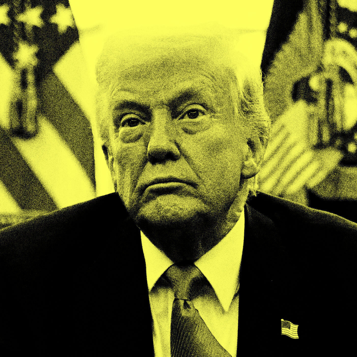 A person in a suit and tie sits in front of American flags, illuminated by a yellow light.